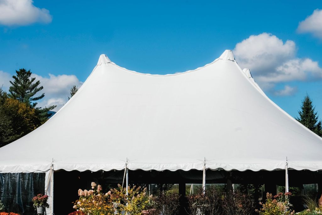 Large white peaked event tent under a blue sky with clouds