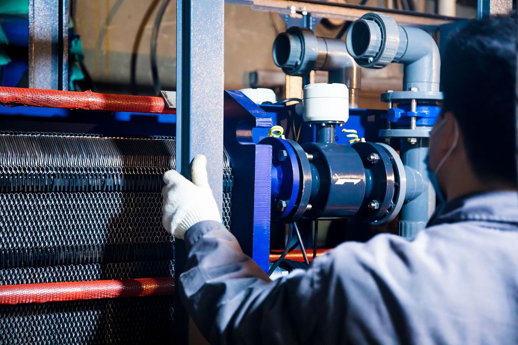 Gloved worker inspecting a heat exchanger and pump piping in a mechanical room